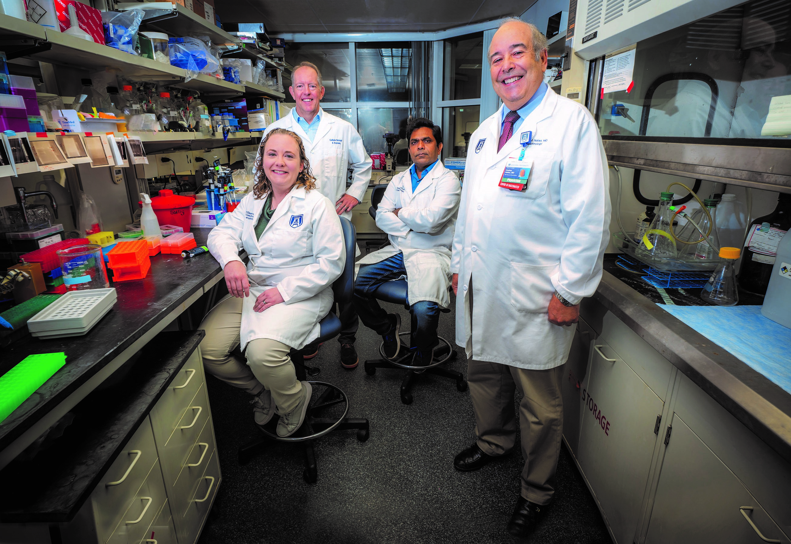 Four people in white coats stand in lab
