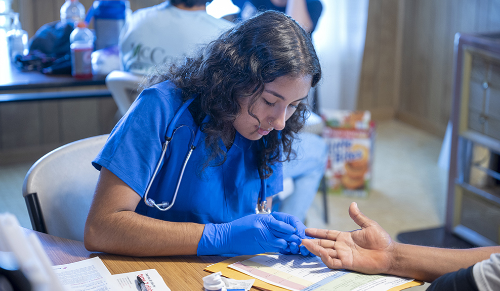 A public health student checks a child's heart with her stethoscope.