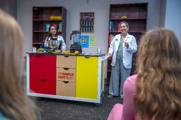 Picture of a mobile field kitchen, a rectangular rolling cart that includes a microwave oven, fruits and vegetables, storage drawers, and a small stovetop