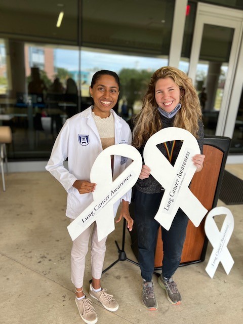 Two womeh holding a white wooden ribbon