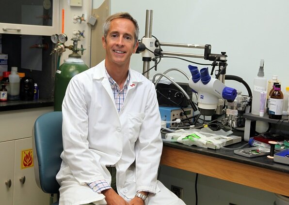 Dr. Belin de Chantemele sitting in his lab next to his microscope