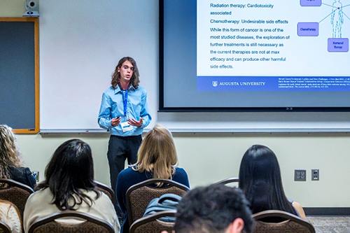 Student standing in front of screen presenting in front of a classroom.