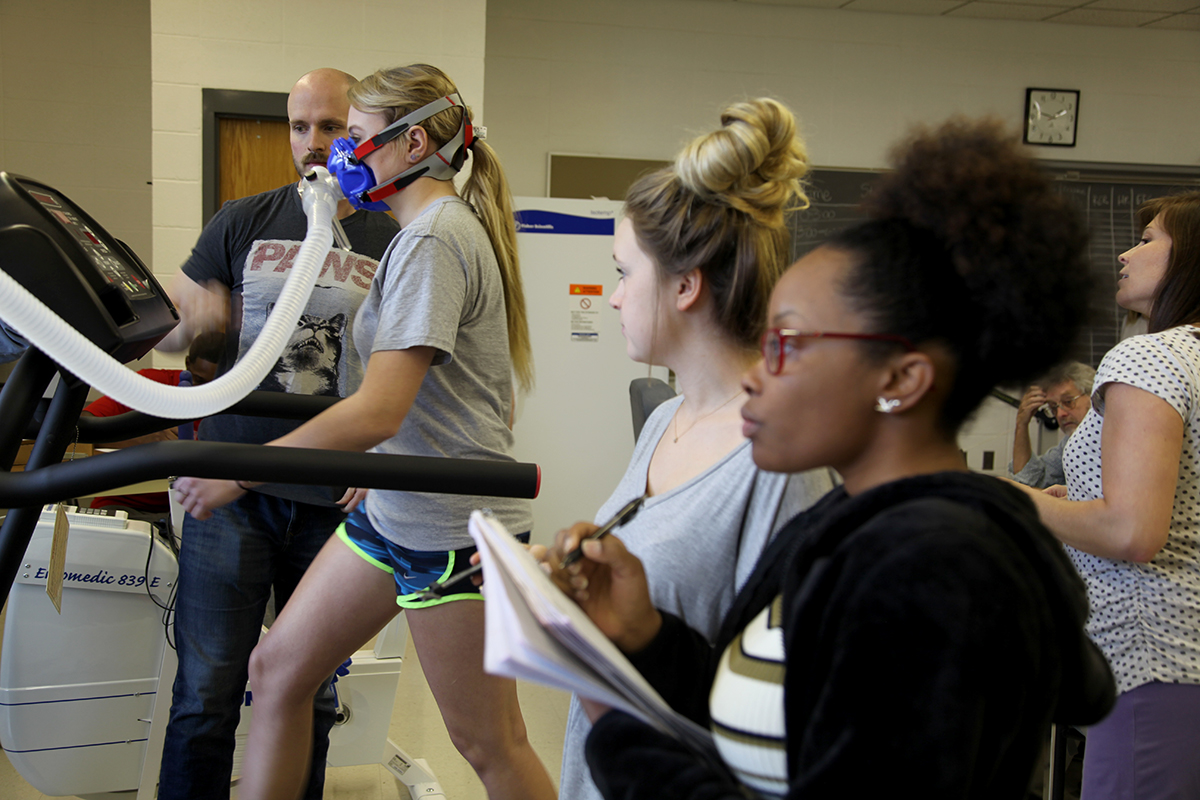 Kinesiology students measure respiration rate and blood oxygenation for a runner on a treadmill.