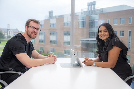 Two students sit at a table and pose for camera