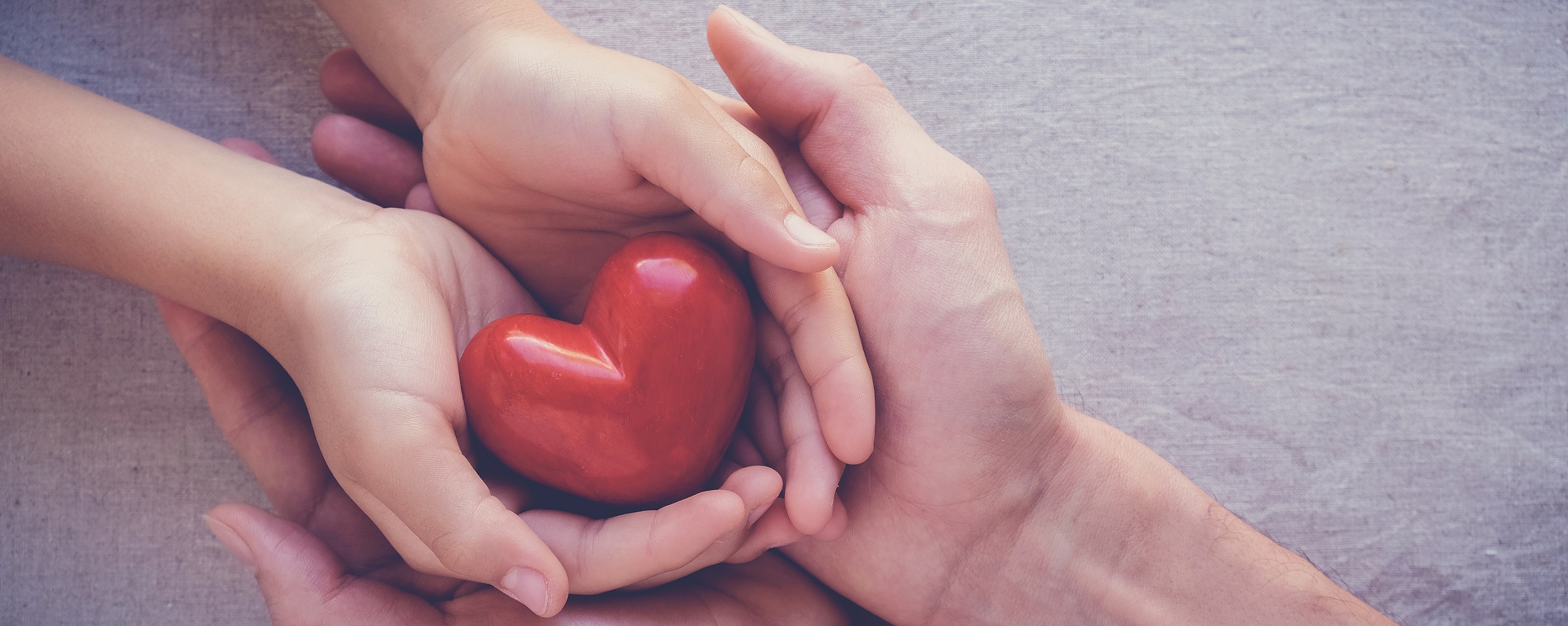 Hands laying on each other holding a red heart