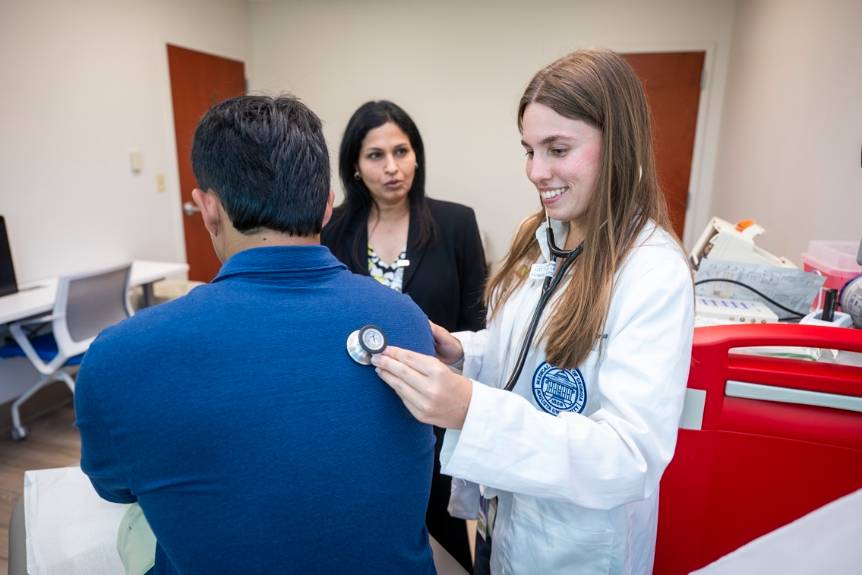Student using a stethoscope with Dr. Loveet, Dr. Anand and another student looking on.
