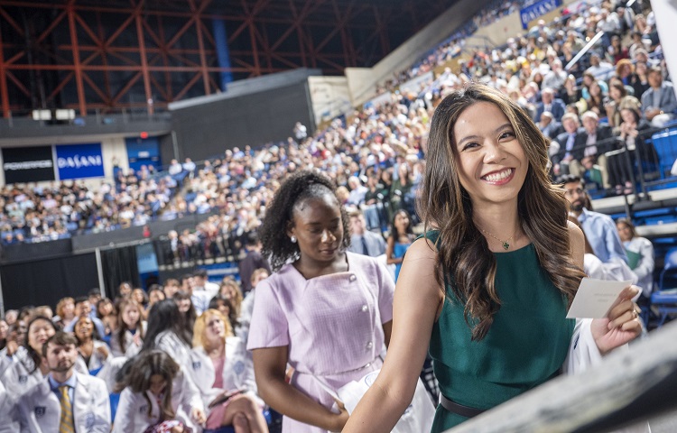 People sitting in the audience and a young woman smiling at the camera at the White Coat Class of 2027