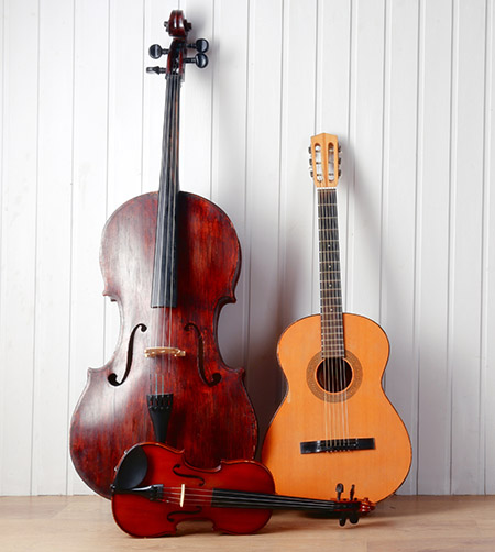 A cello, guitar and violin leaning against a white paneled wall.