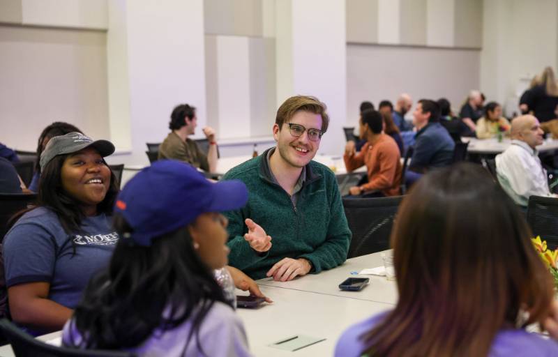Students seated around a table speak with one another