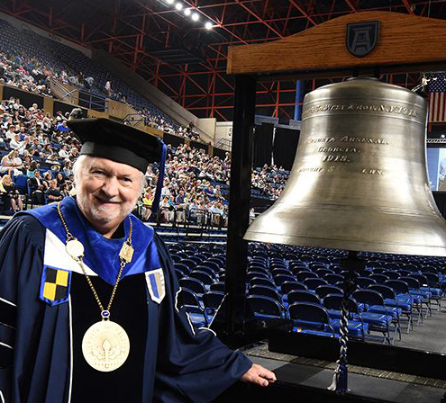 President Keel stands beside Commencement bell at James Brown Arena
