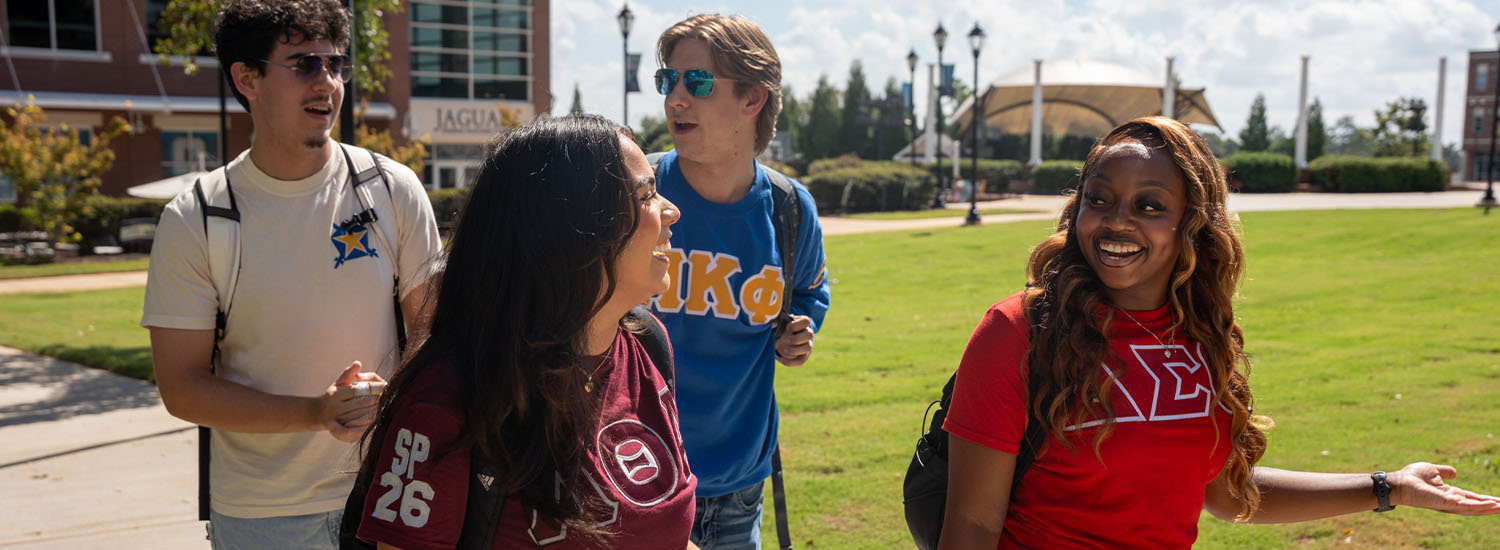 four students walking through campus with fraternity and sorority shirts 