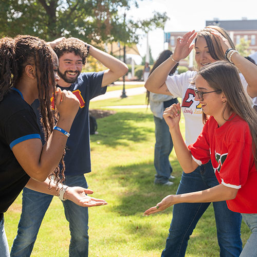 Two students play a game while two other students behind cheer on