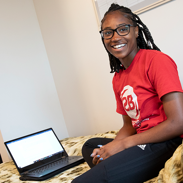 Female student sitting on bed with a laptop computer