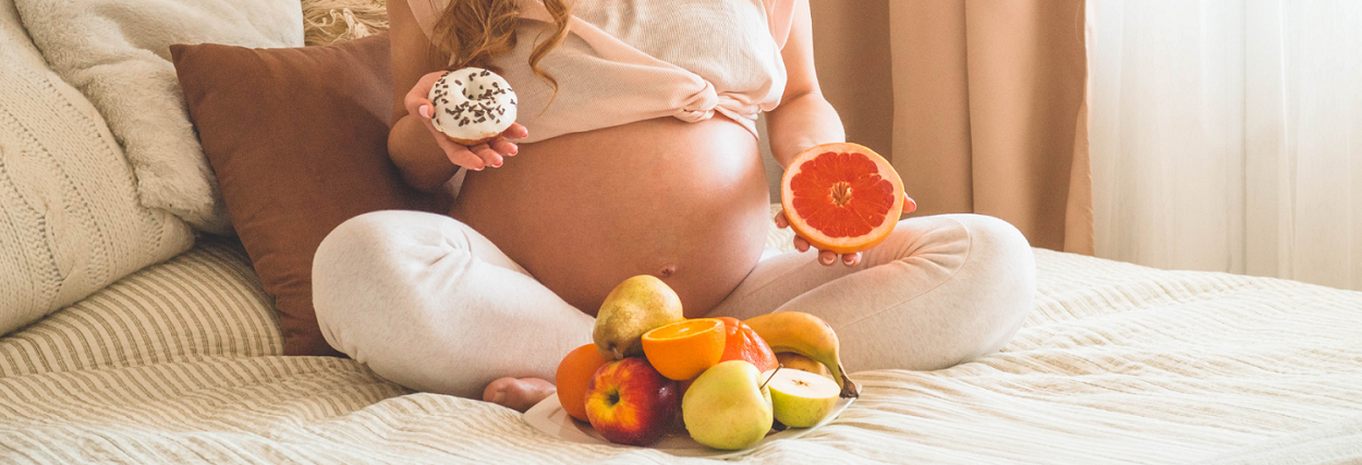 pregnant woman holding fruit and a donut