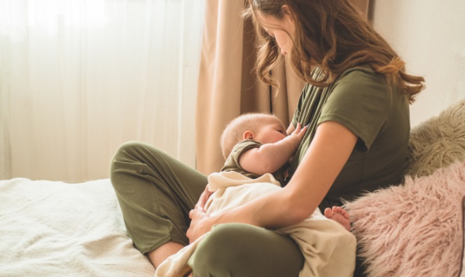 Mother breastfeeding her child sitting on a bed.