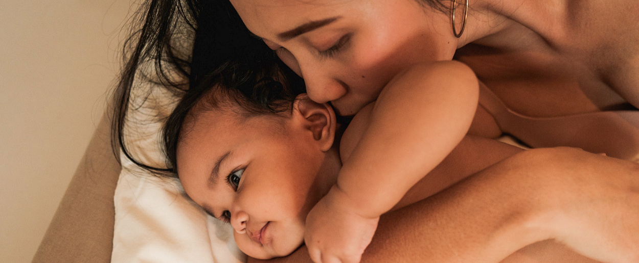 postpartum woman cuddles and kisses her infant