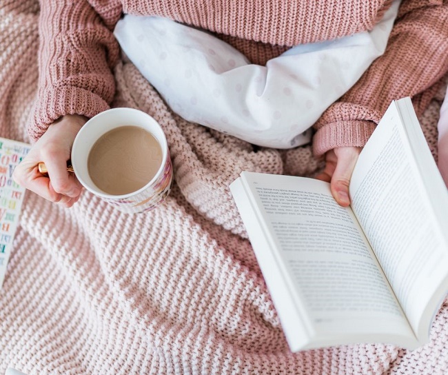 woman reading and drinking tea in bed