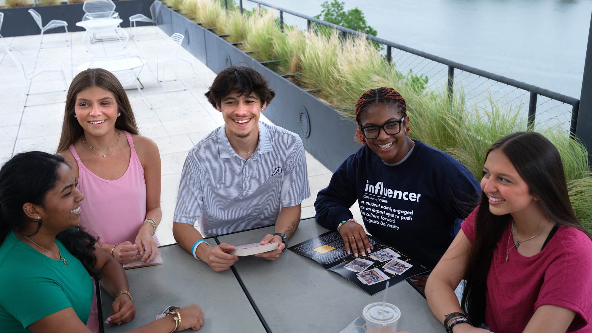 Five Augusta University students collaborate at an outdoor table overlooking the river.
