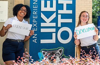 Two students smiling and holding signs that read 'friendship' and 'development'