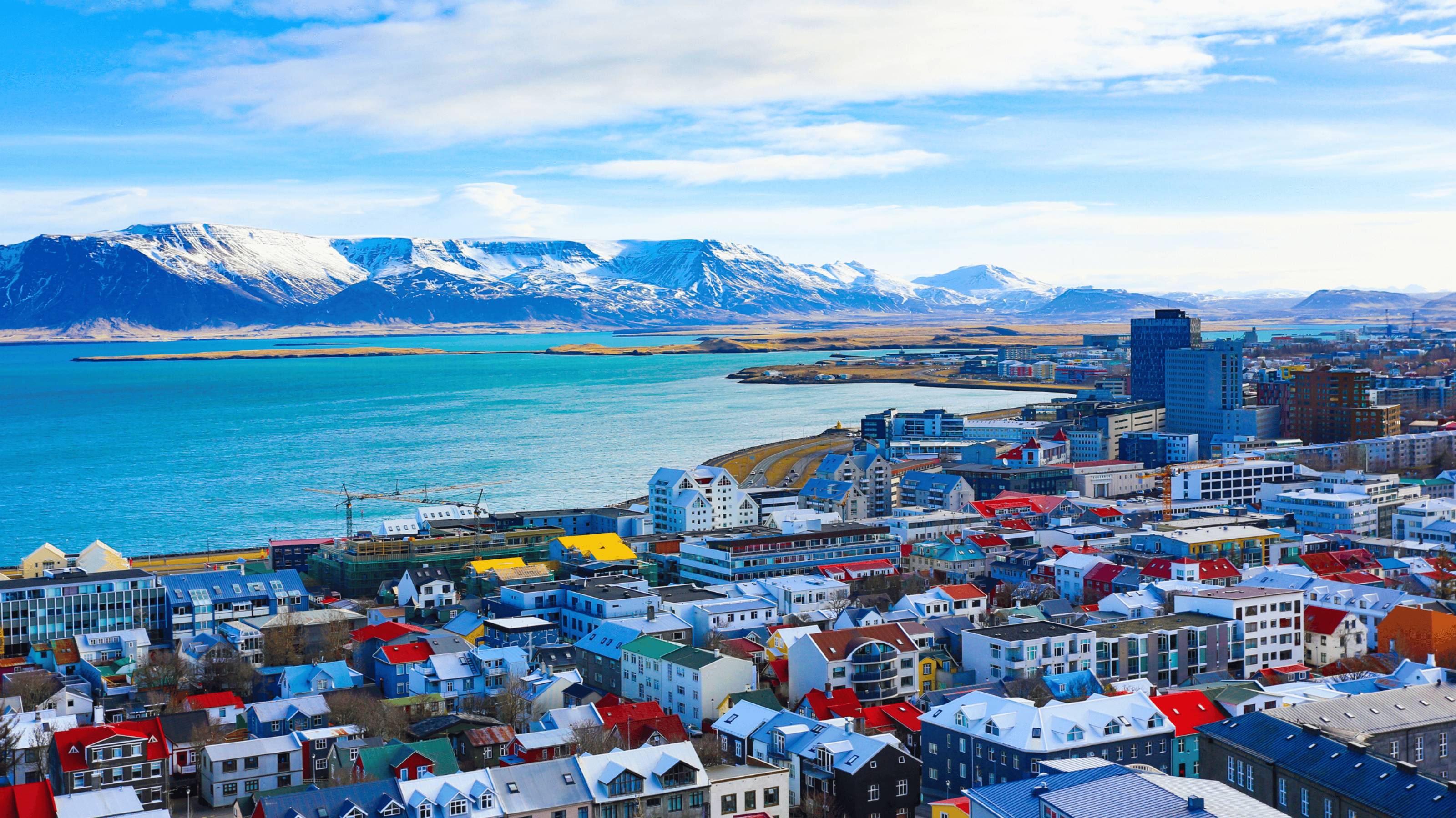 a city overlooks the sea with a snowy mountain in the background