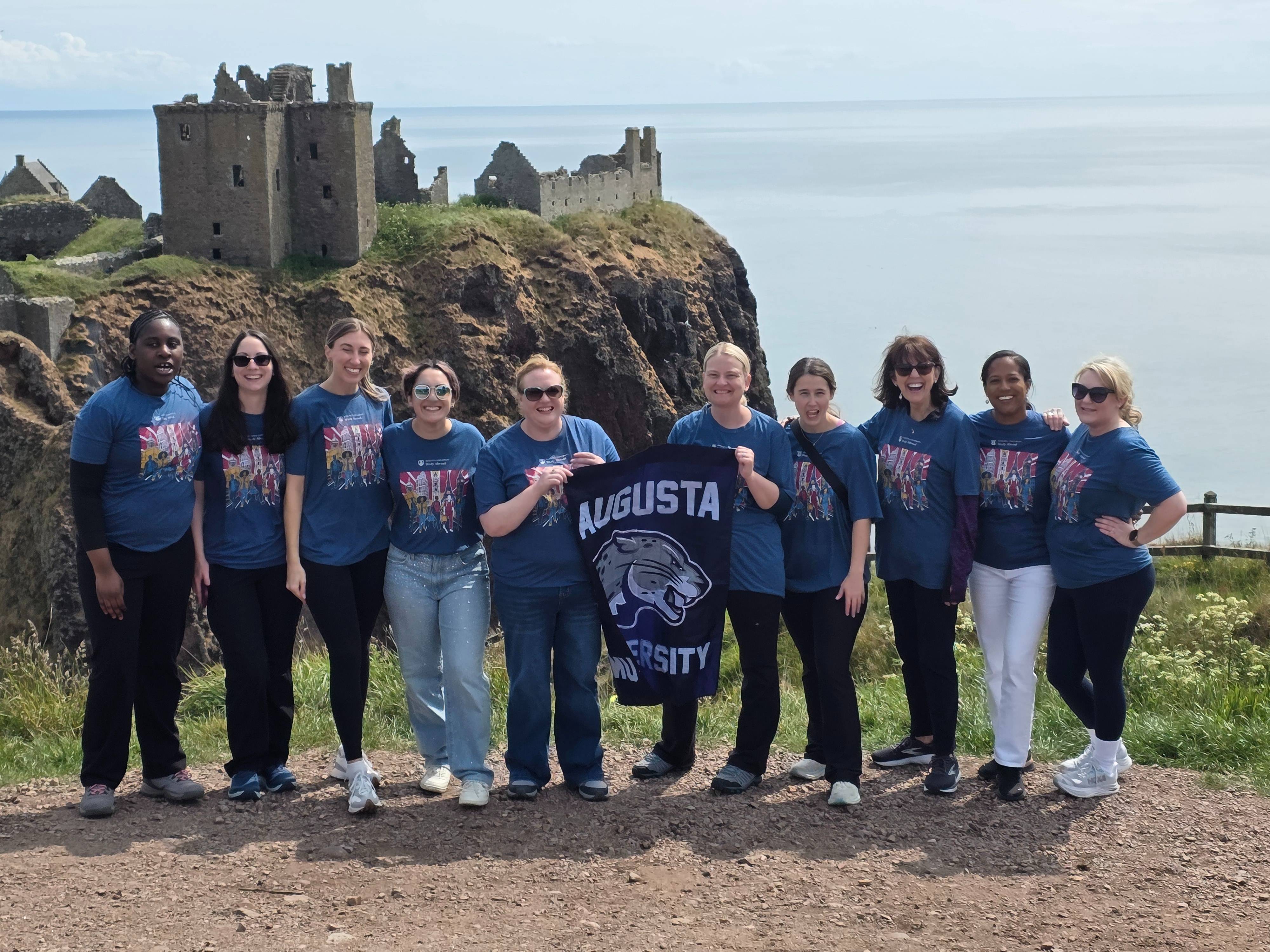 group holds flag in front of castle and waterfront