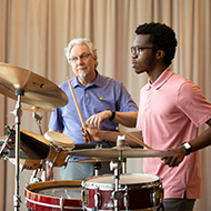 Stduent drumming with the help of his professor