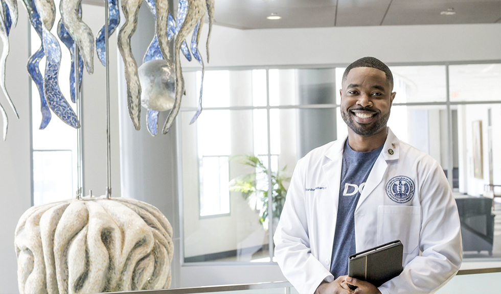 A dental student stands in the lobby by a tooth sculpture